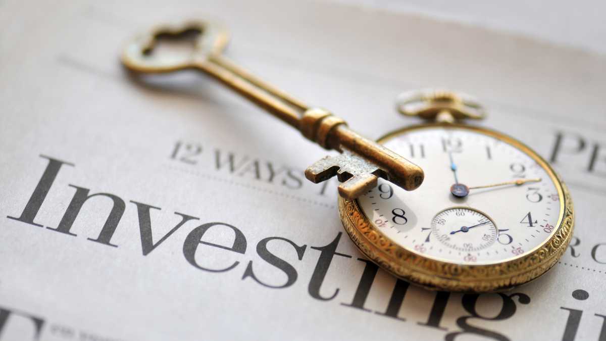 Vintage key and watch on "Investing" text; time and investing concept.