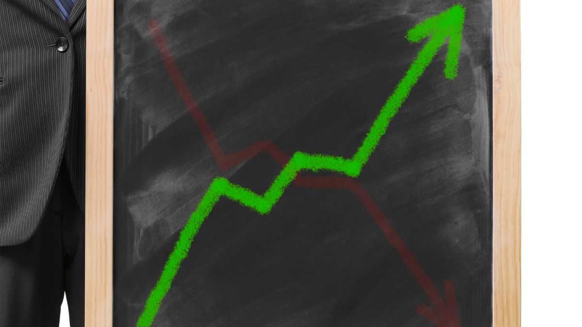 A person in a suit pointing to a chalkboard with a green upward trending graph