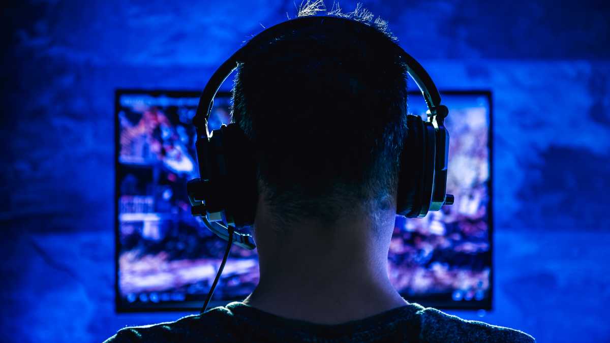 Rear view of a person with headphones gaming in front of blue lit screens