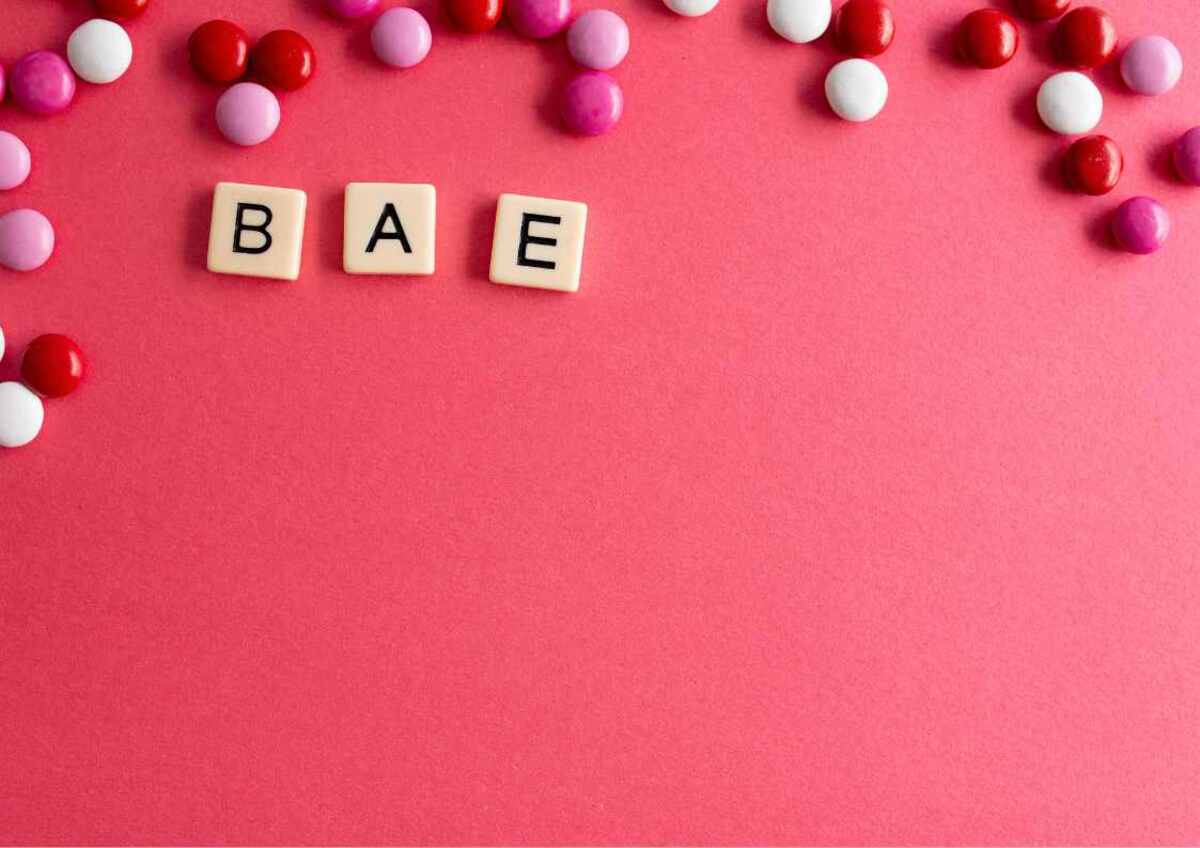 Letter tiles spelling "BAE" surrounded by colourful candies on a pink background.