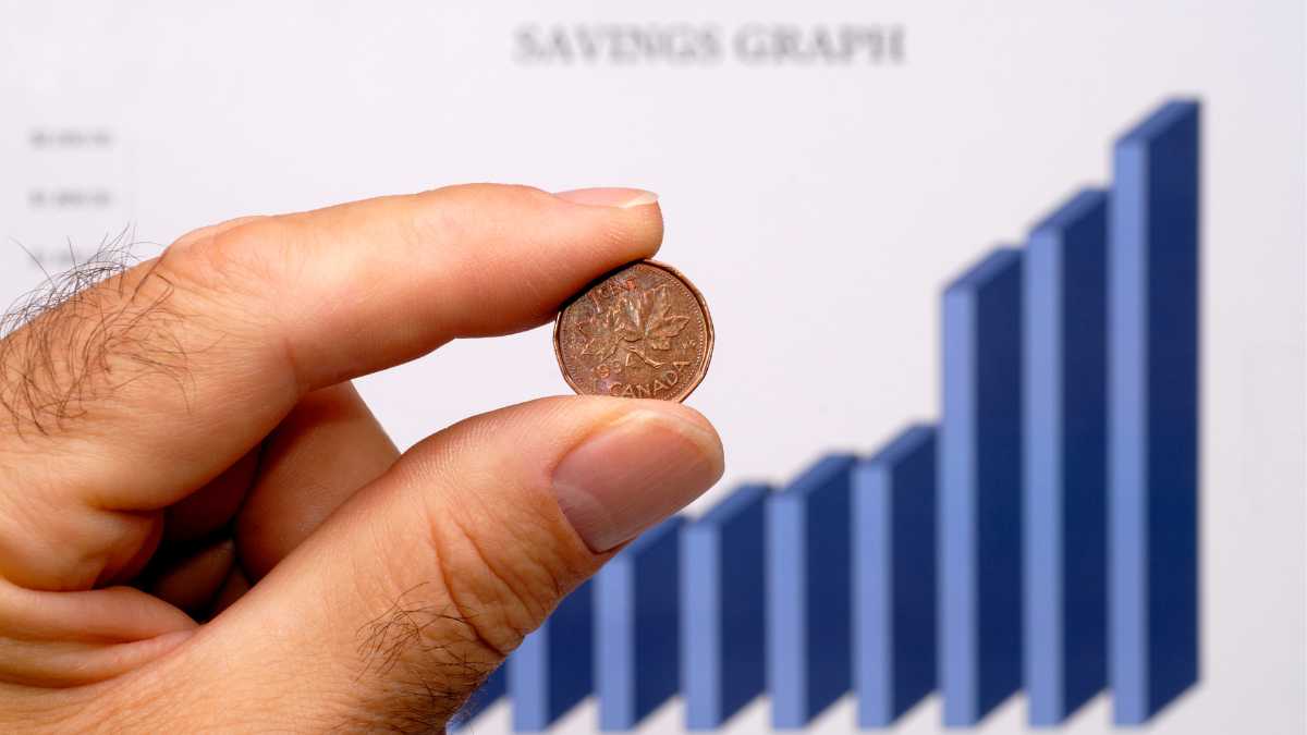 Hand holding a Canadian penny against a financial graph background