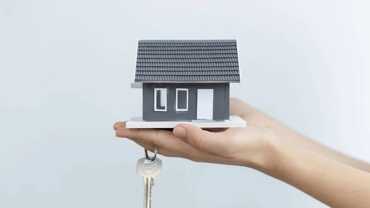 a hand holding a small model of a house with a set of keys dangling from the roof