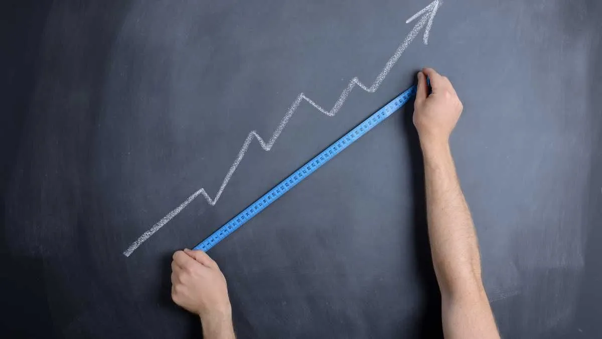 Hand drawing an upward trend line with a ruler on a chalkboard