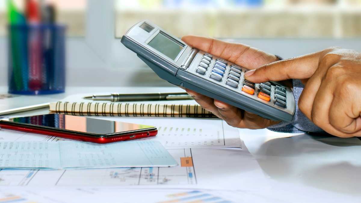 The image shows a person's hand holding a calculator over financial documents