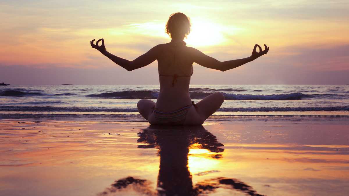 Person meditating on the beach at sunset