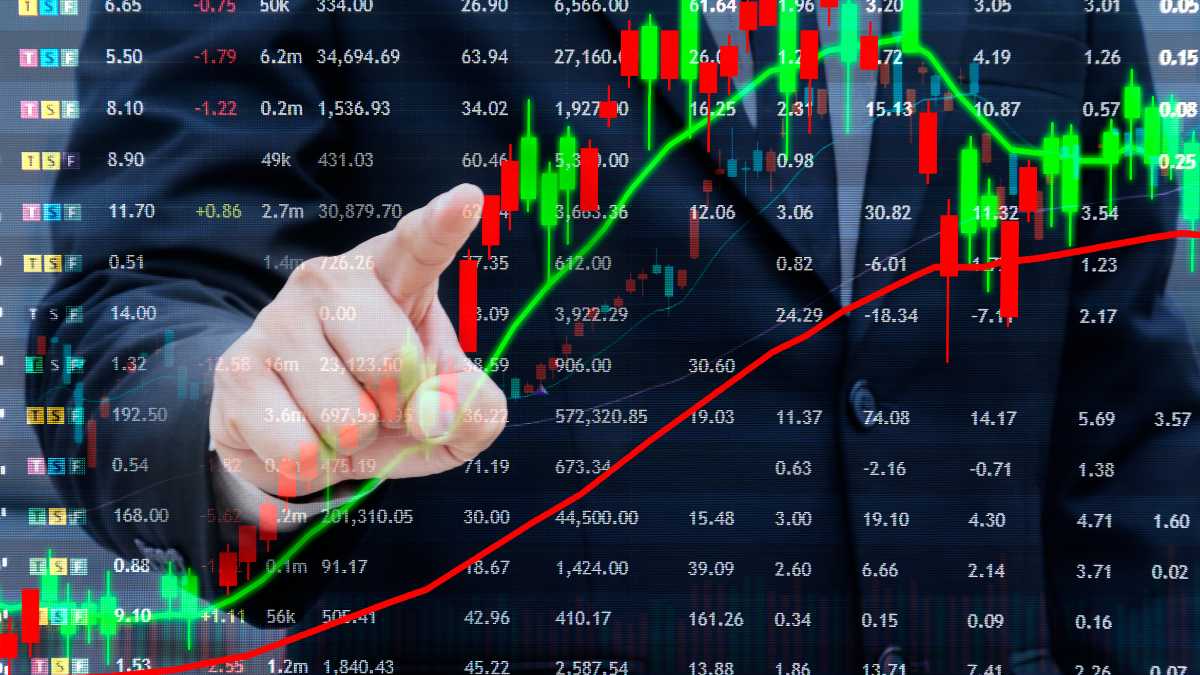 Finger pointing at stock market candlestick graph with red and green bars.