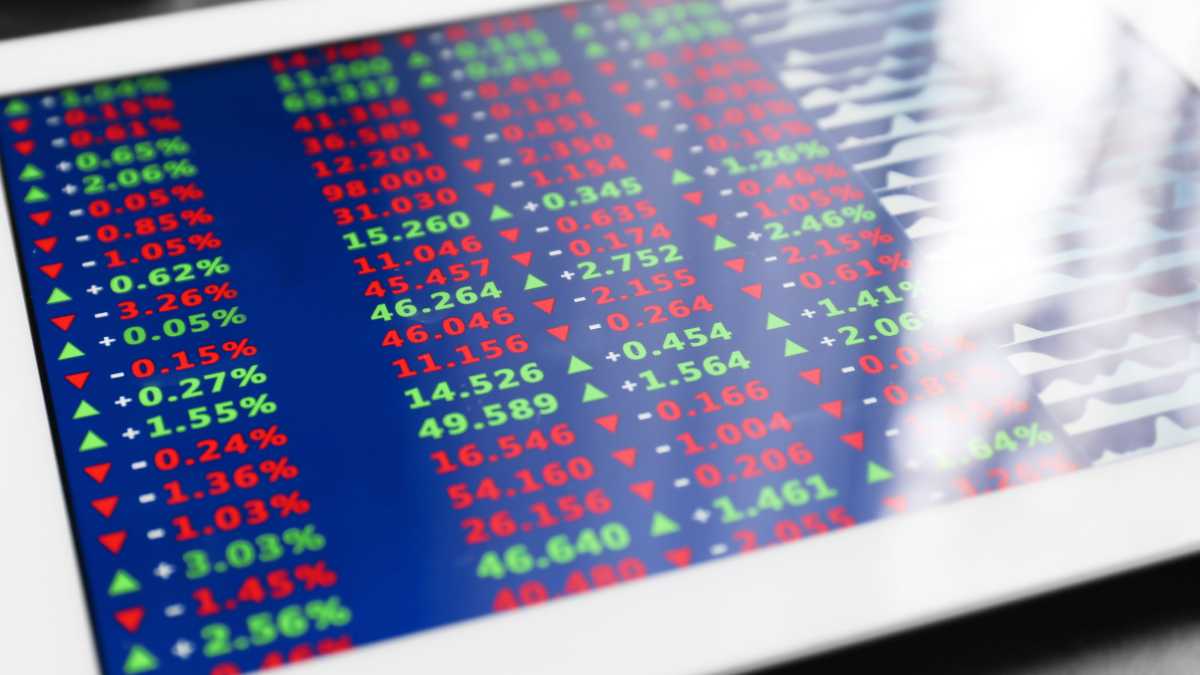 A stock market display shows various stock prices with red and green arrows indicating market movements.