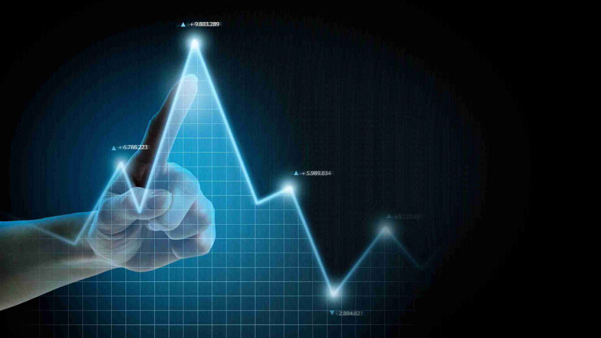 A finger precisely pointing at the peak of a trading chart