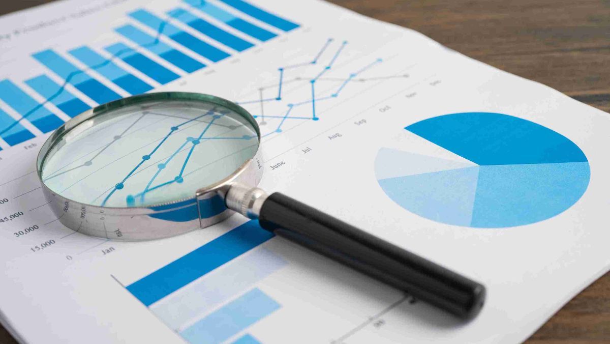 A magnifying glass examining documents adorned with graphs and charts