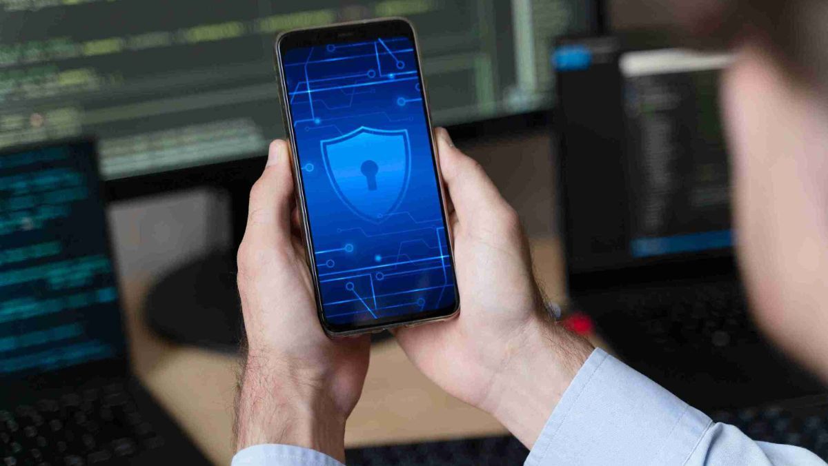 A man firmly holds a mobile phone displaying a security logo