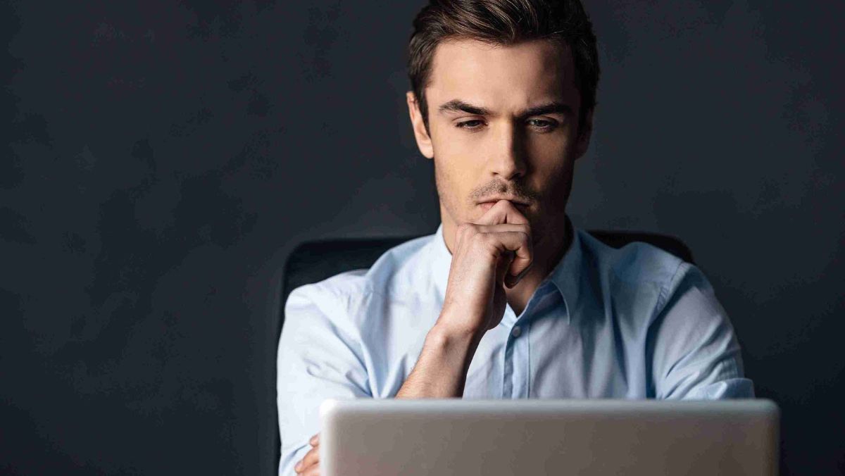 A man pondering intensely while seated in front of his laptop