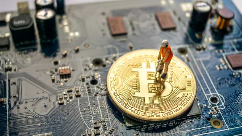 A miniature figure mining a Bitcoin coin on a motherboard