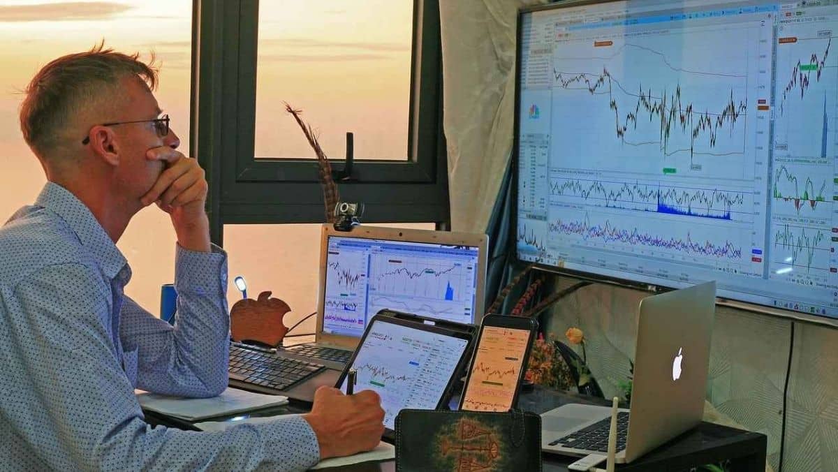 A person carefully studying trading charts, surrounded by multiple open screens