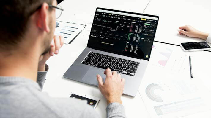 A man doing technical analysis on a laptop over printed finance charts