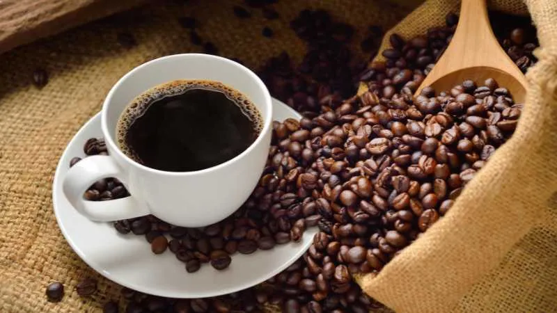 Cup of black coffee with beans on burlap cloth