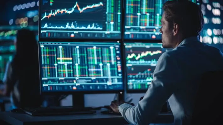 A man analysing data on multiple computer monitors