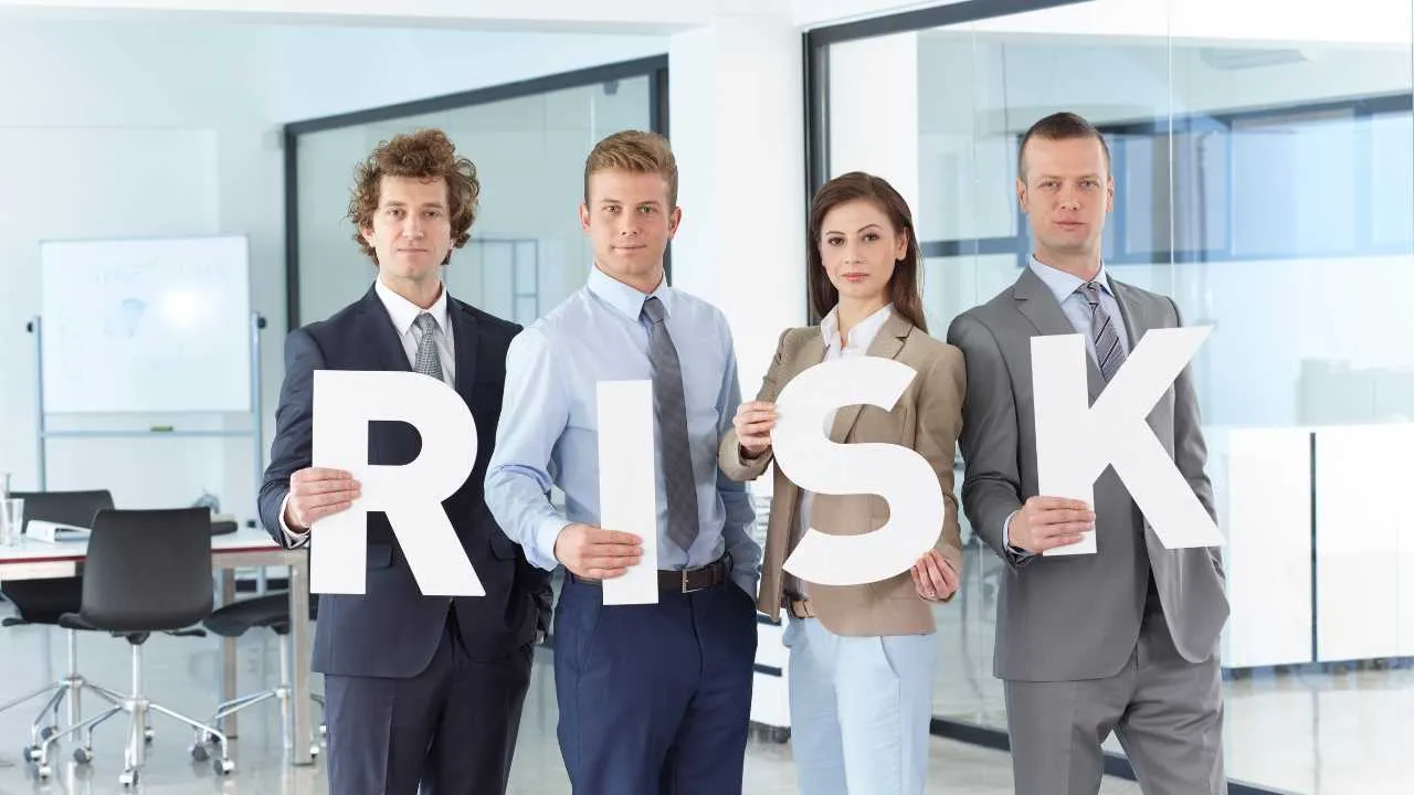 Four professionals holding up letters spelling RISK in an office setting 