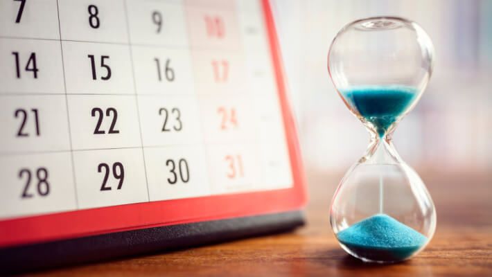 Hourglass with blue sand and calendar in background