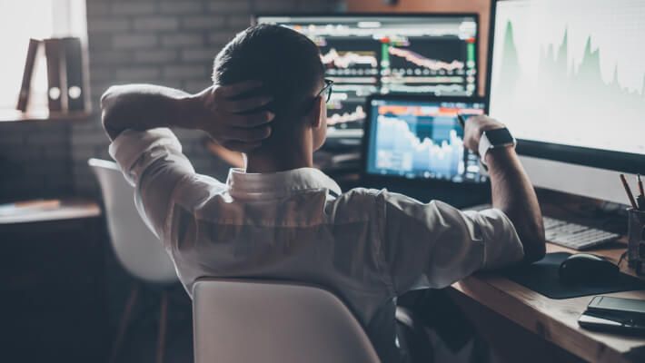 Man at desk with multiple screens displaying financial charts