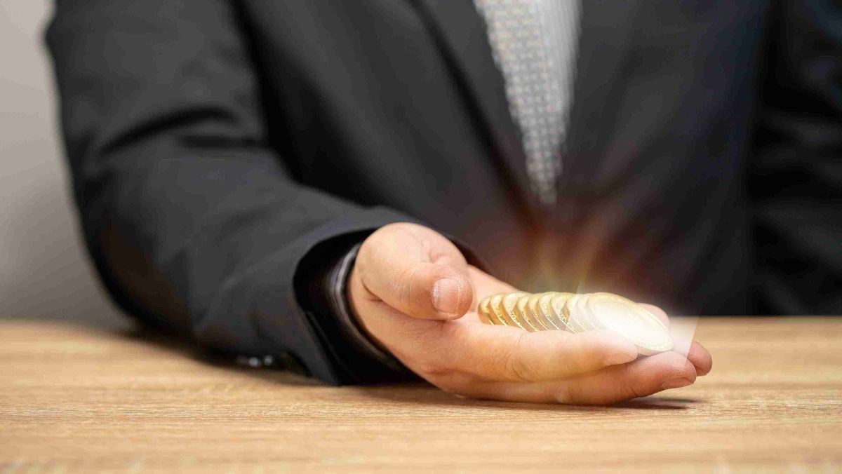 Man's arm on the table holds a handful of gold coins