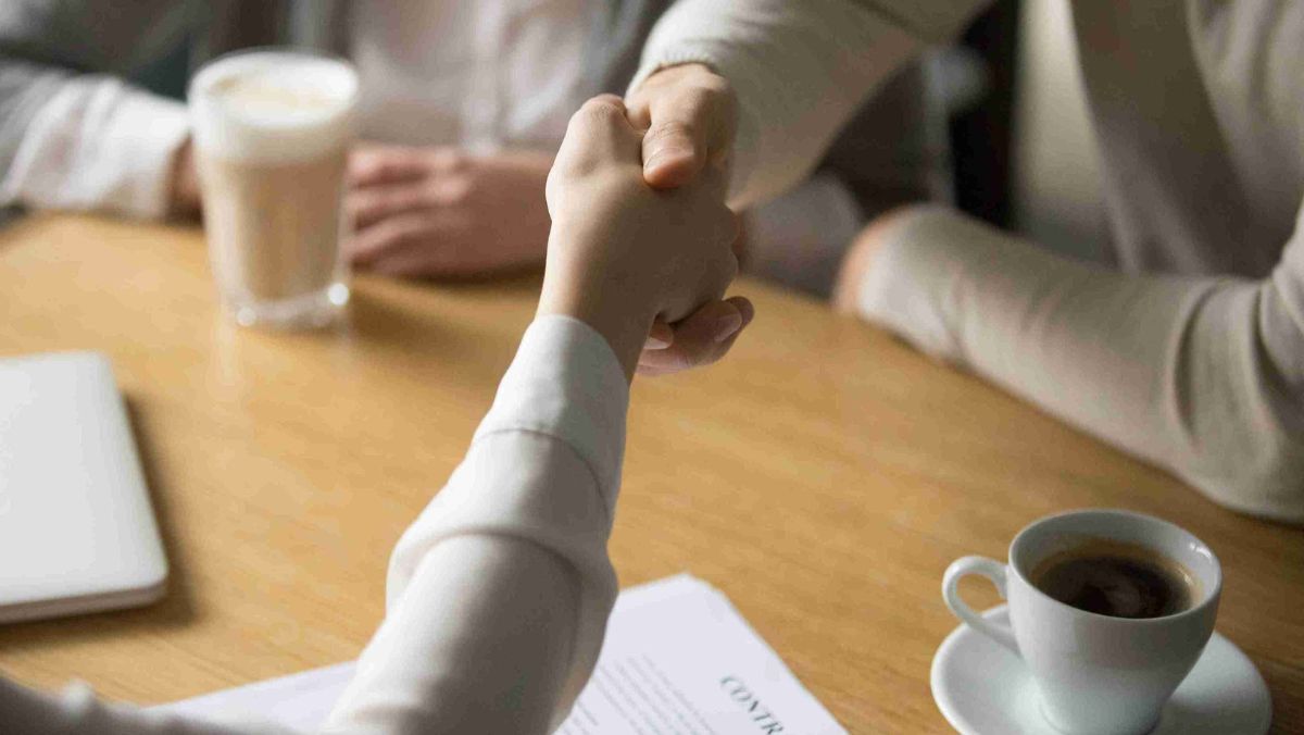 Mutual agreement portrayed as two people shaking hands over a document.