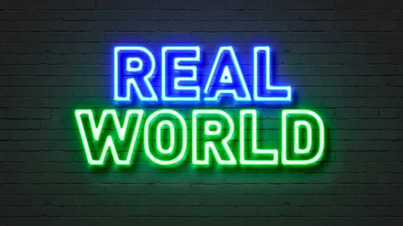 Neon sign on brick wall reads REAL WORLD in blue and green