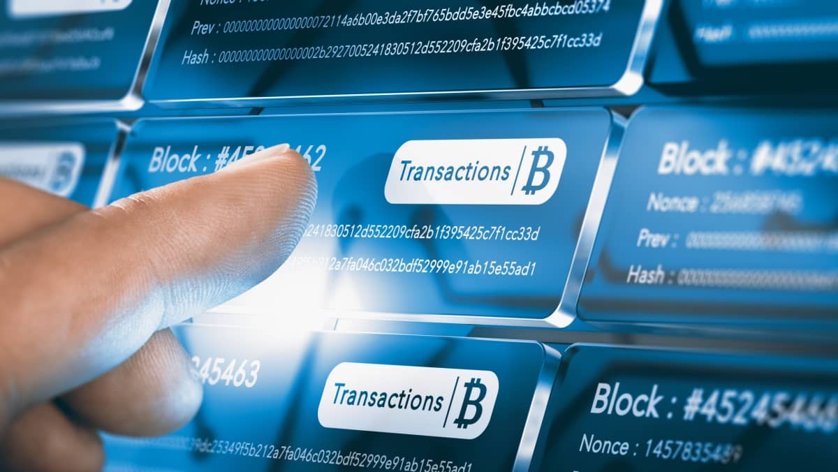 Finger touching a blockchain block with the text transaction prominently displayed