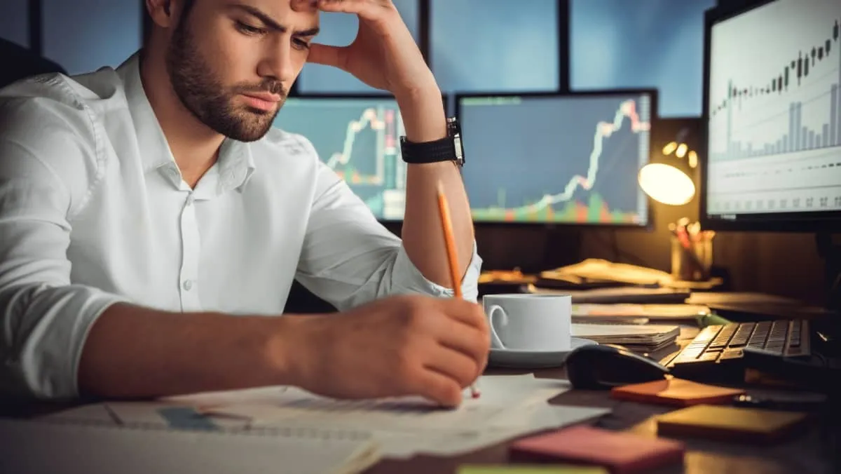 A focused trader solving problems, working diligently with a computer and piles of documents in the office