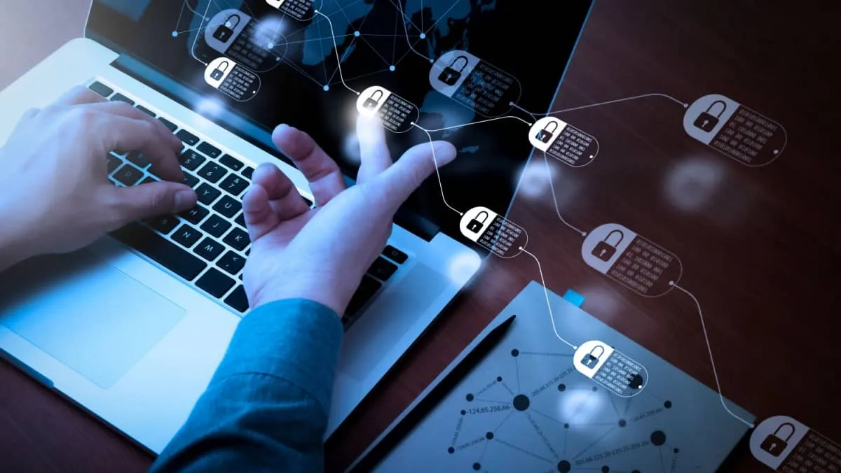 A man seated at an office table with his laptop surrounded by a diagram of chains and encrypted blocks