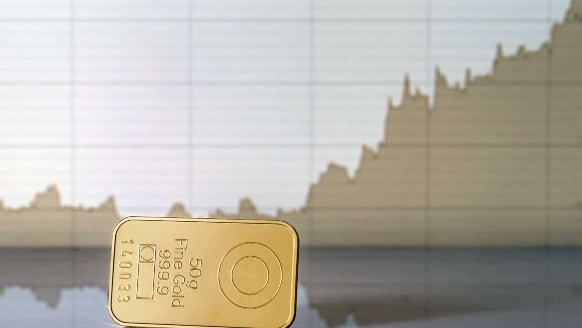 A 50 grams fine gold bar is placed on the table with a graph in the background displaying a clear ascending direction