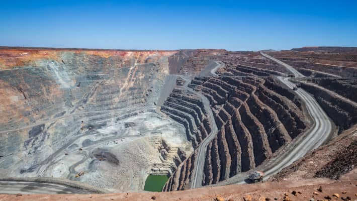 Aerial view of an expansive open-pit mine with terraced layers, a central water body, and surrounding infrastructure