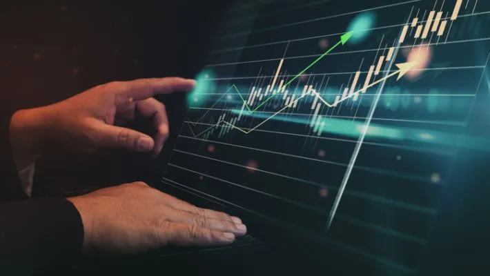 a trading chart showing the time period, a hand holding a pen pointing at the tablet’s screen