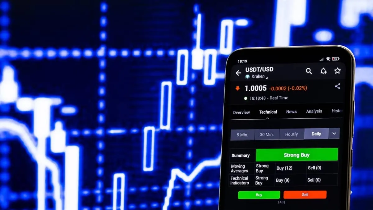 Smartphone displaying a USDT USD trading platform with lively blue hued trading charts in the background