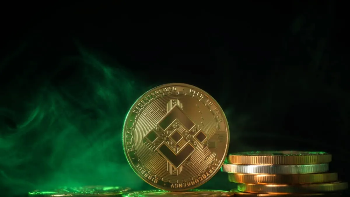 A golden Binance coin standing next to a pile of similar coins set against a backdrop of smoky green