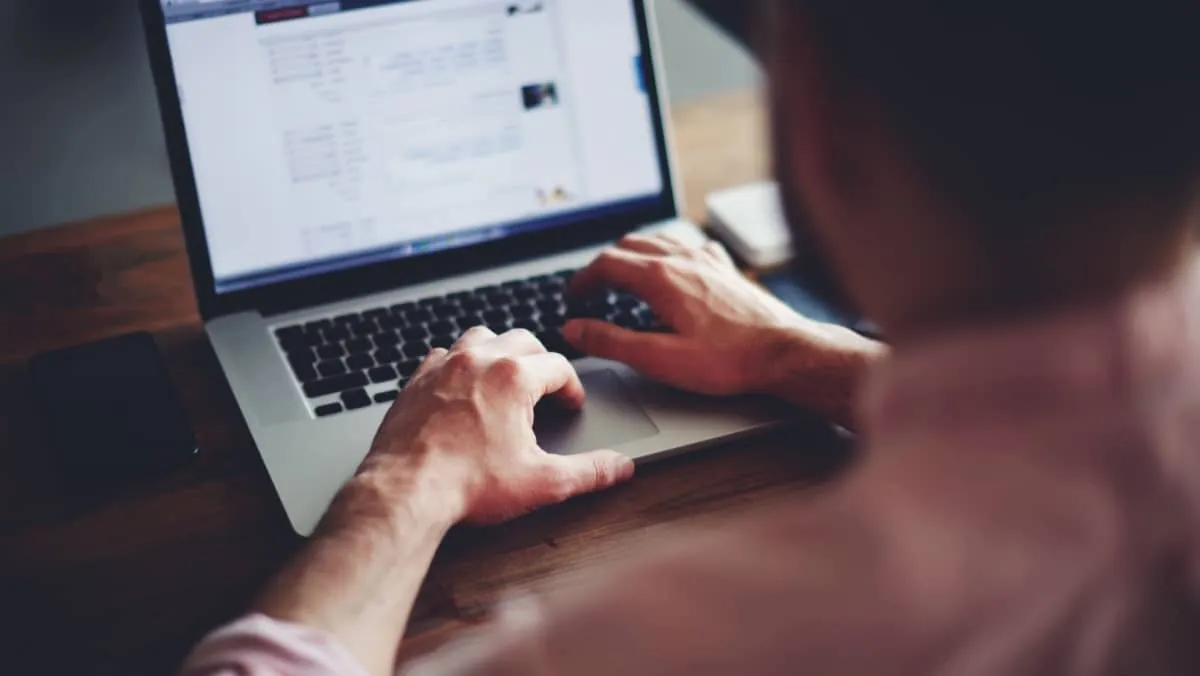 A cropped shot of a man intensely focused on his laptop that is placed on a wooden table