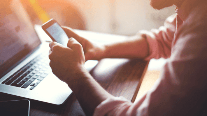 Silhouette of a young man fully immersed in his work using a smartphone and notebook computer