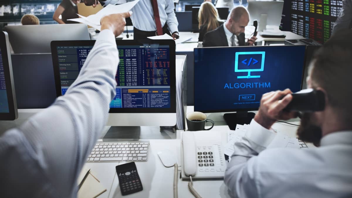 Busy office with collaborative work stock market screen on the right and multiple computers in use