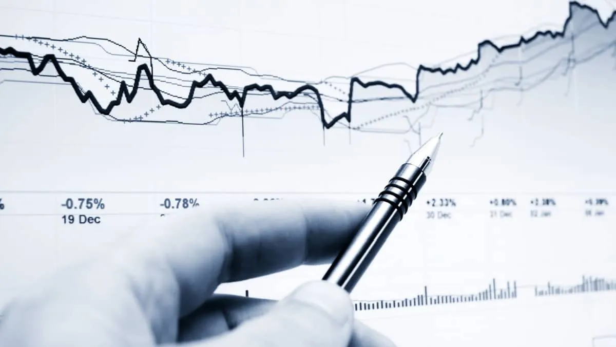 Monochrome image capturing a hand with a pen pointing at a line graph