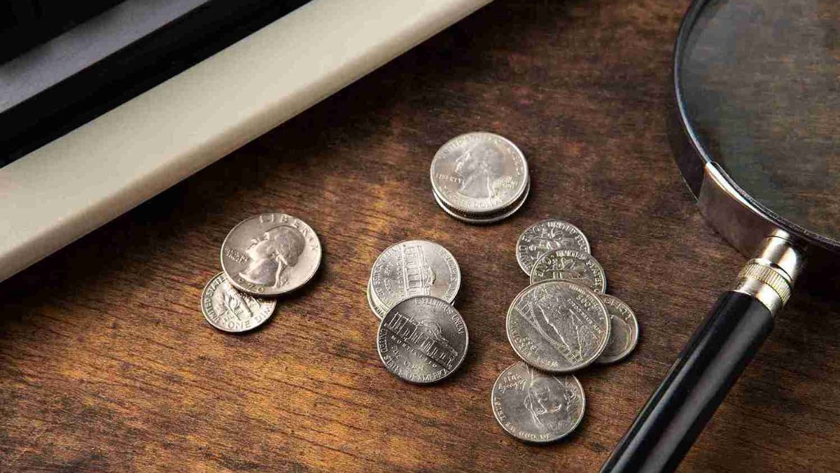 Silver coins scattered on the table alongside a magnifying glass