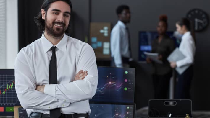 professional young trader smiling while standing with his arms crossed in the office