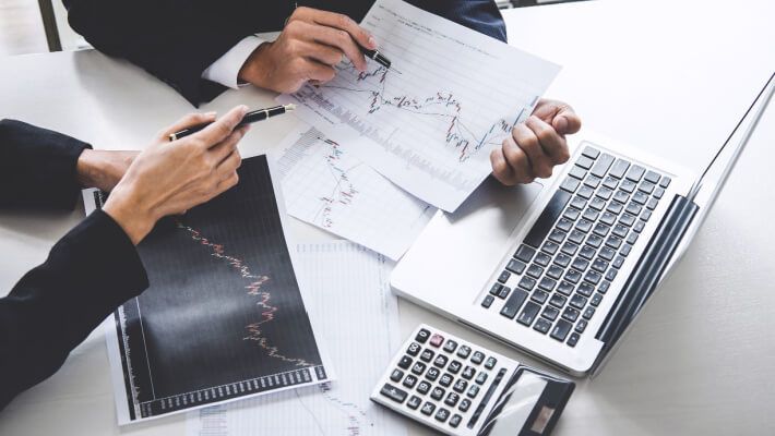 Two people analysing financial charts on paper and a laptop