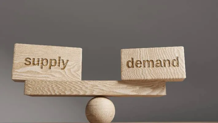 blocks labeled “Supply” and “Demand” balanced on a wooden seesaw