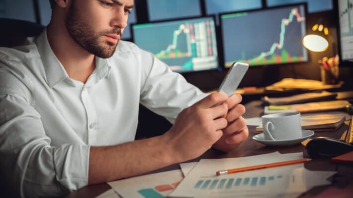 A person is analysing financial charts on a laptop and mobile phone.